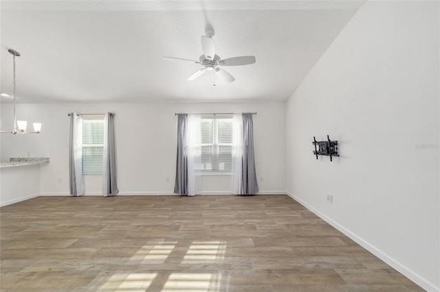 unfurnished room with ceiling fan with notable chandelier, light hardwood / wood-style floors, and plenty of natural light