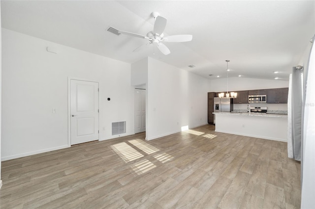 unfurnished living room with ceiling fan with notable chandelier, light hardwood / wood-style floors, vaulted ceiling, and sink