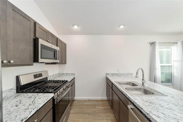 kitchen featuring appliances with stainless steel finishes, dark brown cabinetry, sink, light hardwood / wood-style flooring, and lofted ceiling