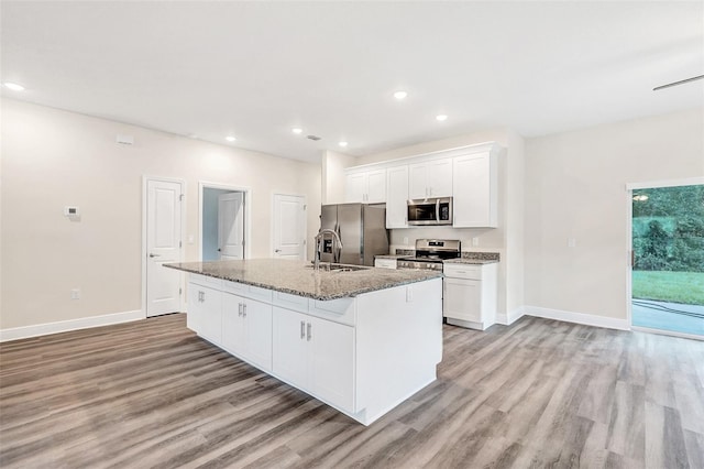 kitchen with white cabinets, light wood-type flooring, a center island with sink, and stainless steel appliances