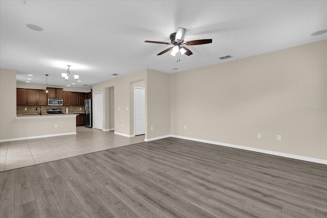 unfurnished living room featuring ceiling fan with notable chandelier, sink, and light hardwood / wood-style flooring