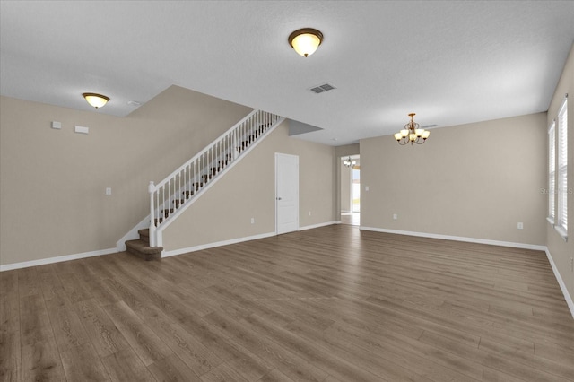 unfurnished living room with a chandelier, a healthy amount of sunlight, a textured ceiling, and hardwood / wood-style flooring