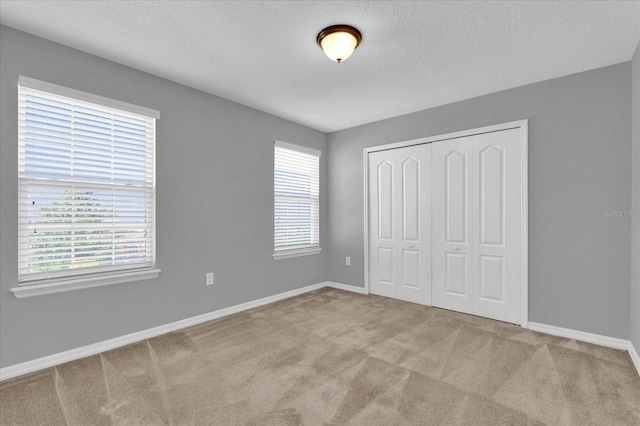 unfurnished bedroom with a closet, light colored carpet, a textured ceiling, and multiple windows