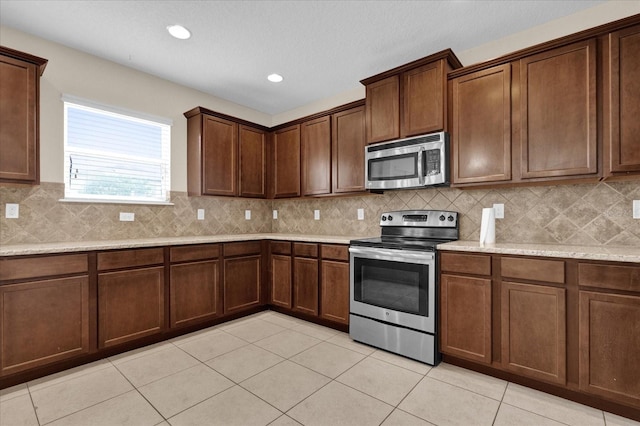 kitchen with light stone countertops, light tile patterned floors, tasteful backsplash, and appliances with stainless steel finishes