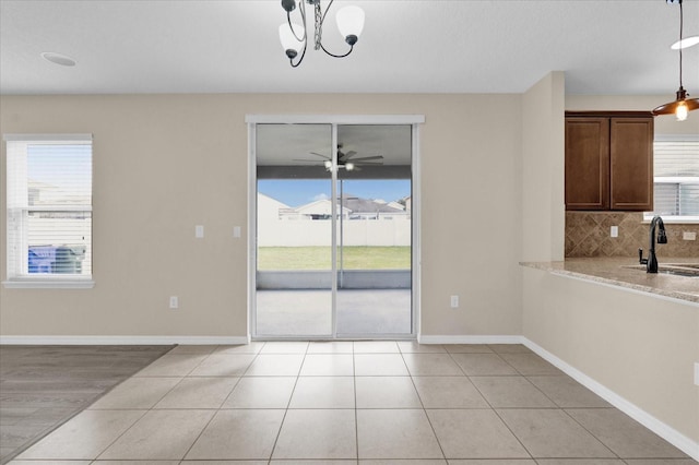 unfurnished dining area with a sink, light tile patterned floors, baseboards, and a ceiling fan