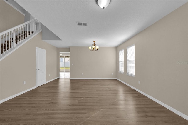 unfurnished room with dark wood-style floors, baseboards, visible vents, and an inviting chandelier