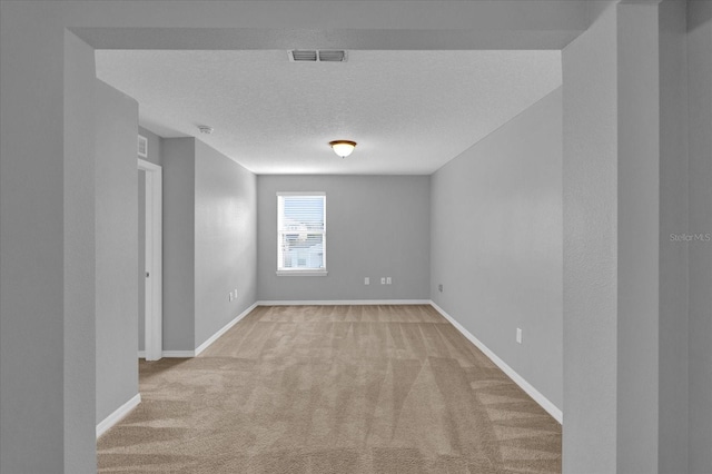 unfurnished room with light carpet, a textured ceiling, visible vents, and baseboards