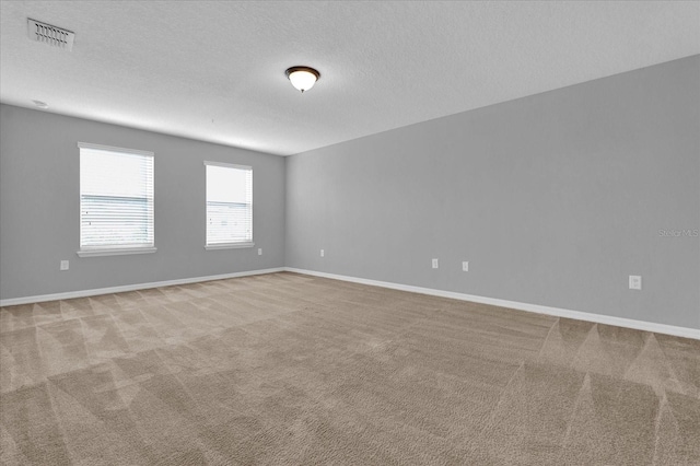 unfurnished room with a textured ceiling, baseboards, visible vents, and light colored carpet