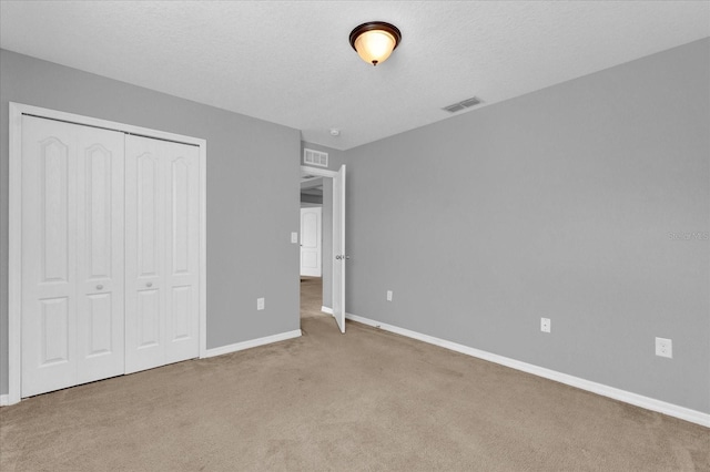 unfurnished bedroom featuring a textured ceiling, visible vents, baseboards, a closet, and carpet