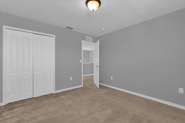 unfurnished bedroom featuring light colored carpet, a closet, visible vents, and a textured ceiling