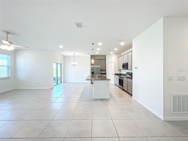 kitchen with appliances with stainless steel finishes, ceiling fan, light tile patterned floors, a center island with sink, and decorative light fixtures