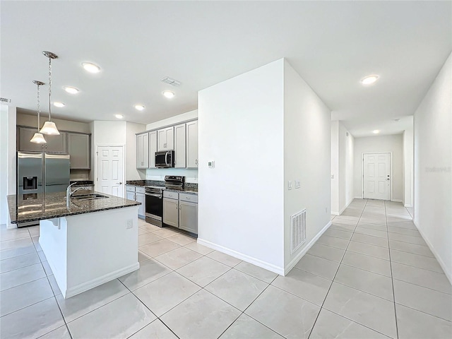 kitchen with sink, hanging light fixtures, stainless steel appliances, an island with sink, and dark stone counters