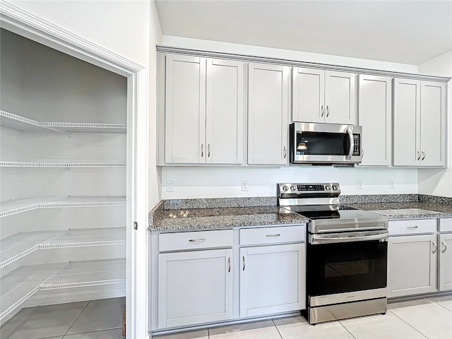 kitchen featuring gray cabinets, light tile patterned floors, stainless steel appliances, and dark stone counters