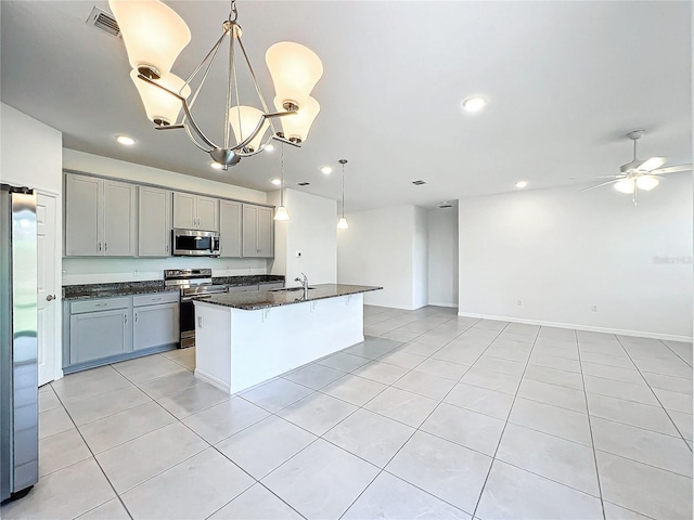 kitchen with a center island with sink, sink, dark stone countertops, decorative light fixtures, and stainless steel appliances