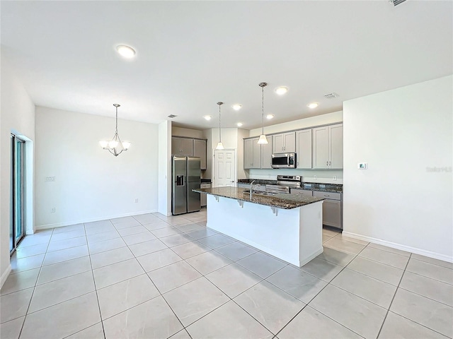 kitchen featuring stainless steel appliances, dark stone countertops, an island with sink, pendant lighting, and a breakfast bar area