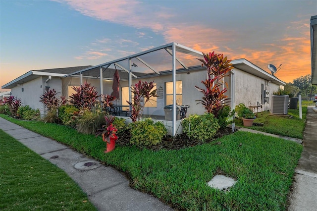 property exterior at dusk with central AC unit, a lanai, and a lawn