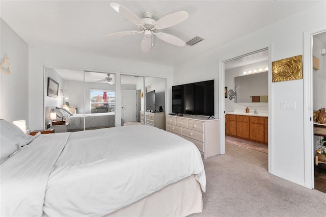 carpeted bedroom featuring ensuite bath, ceiling fan, sink, and multiple closets