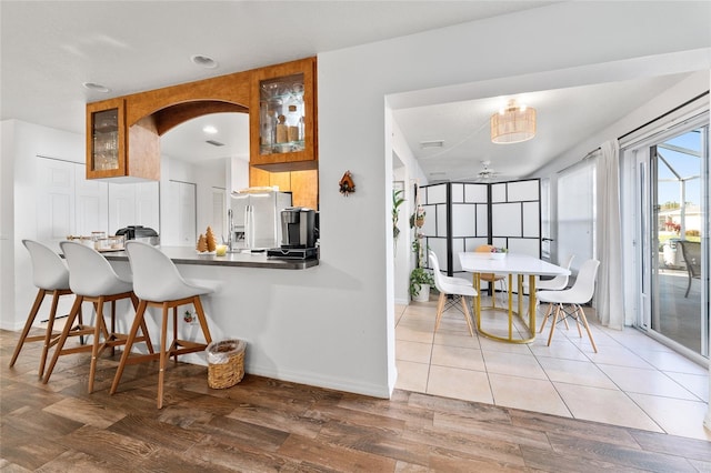 kitchen with ceiling fan, a kitchen breakfast bar, kitchen peninsula, stainless steel fridge, and wood-type flooring