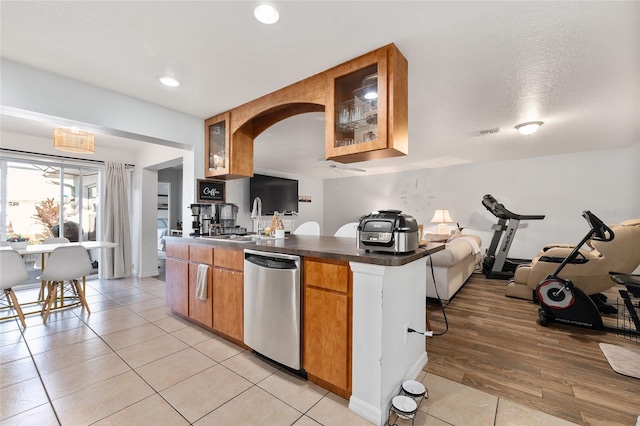 kitchen featuring a textured ceiling, light wood-type flooring, stainless steel dishwasher, and sink