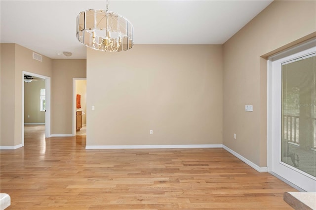 empty room with ceiling fan with notable chandelier and light hardwood / wood-style flooring