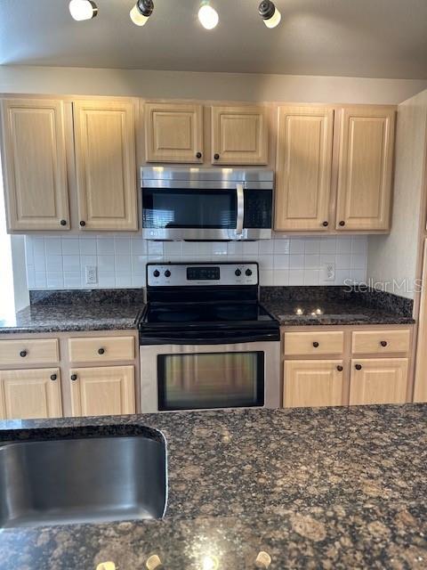 kitchen with dark stone countertops, light brown cabinetry, appliances with stainless steel finishes, and tasteful backsplash