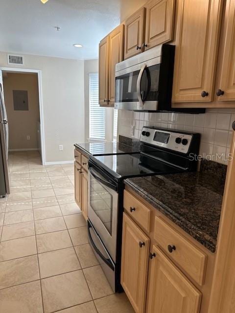 kitchen with backsplash, dark stone countertops, light tile patterned flooring, and stainless steel appliances