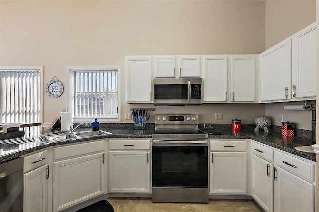 kitchen with a towering ceiling, stainless steel appliances, sink, dark stone countertops, and white cabinetry