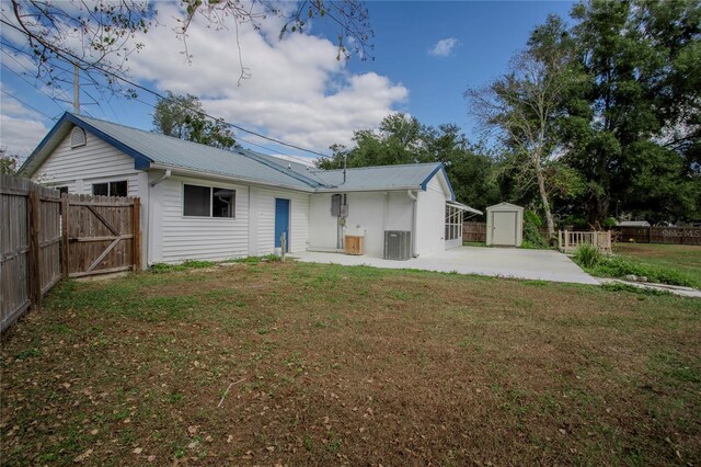 back of property featuring central AC unit, a patio area, a yard, and a storage shed