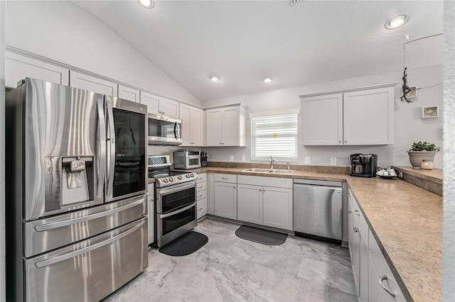 kitchen with sink, a textured ceiling, vaulted ceiling, white cabinets, and appliances with stainless steel finishes