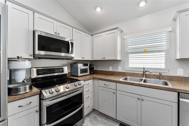 kitchen with a textured ceiling, stainless steel appliances, sink, white cabinets, and lofted ceiling