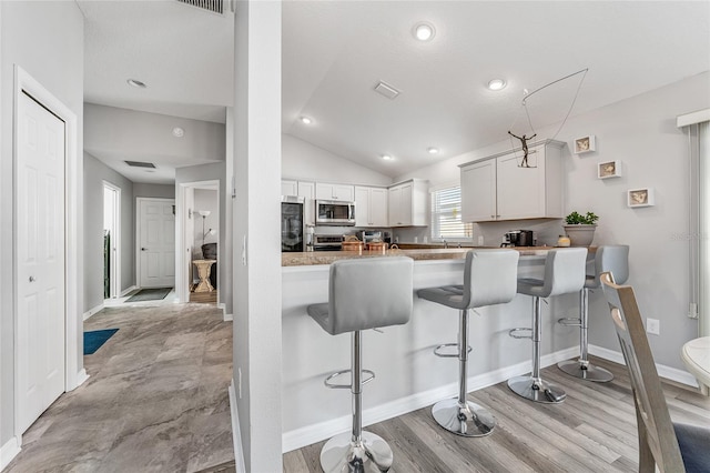 kitchen featuring a breakfast bar area, kitchen peninsula, white cabinets, and lofted ceiling