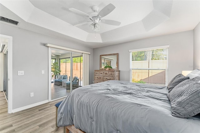 bedroom featuring ceiling fan, multiple windows, access to outside, and a tray ceiling