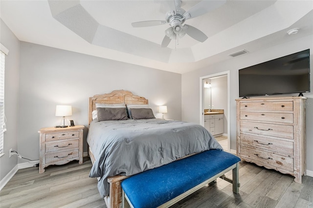 bedroom featuring a raised ceiling, ensuite bath, ceiling fan, and hardwood / wood-style floors