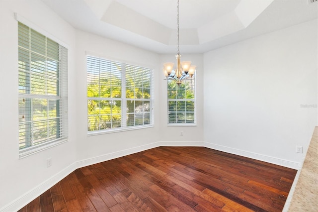 unfurnished room featuring a tray ceiling, a wealth of natural light, an inviting chandelier, and hardwood / wood-style flooring