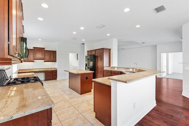 kitchen with black appliances, a center island, light stone countertops, and light hardwood / wood-style floors