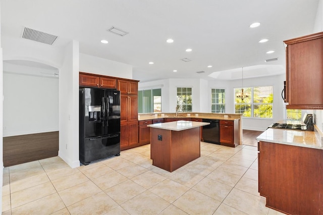 kitchen with light stone countertops, kitchen peninsula, a kitchen island, black appliances, and ceiling fan with notable chandelier