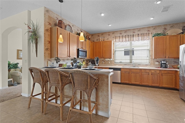 kitchen with stainless steel appliances, a textured ceiling, decorative light fixtures, a kitchen bar, and light tile patterned floors