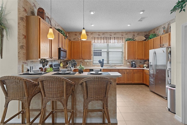 kitchen featuring kitchen peninsula, pendant lighting, a textured ceiling, and stainless steel appliances