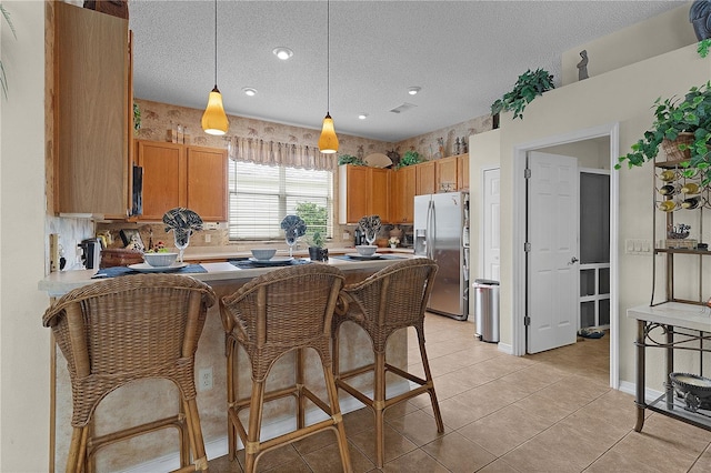 kitchen featuring pendant lighting, stainless steel fridge, a textured ceiling, light tile patterned flooring, and kitchen peninsula