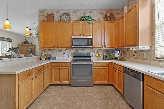 kitchen featuring pendant lighting, light tile patterned floors, a textured ceiling, kitchen peninsula, and stainless steel appliances