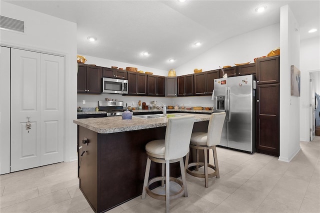 kitchen featuring sink, stainless steel appliances, vaulted ceiling, a kitchen bar, and a center island with sink