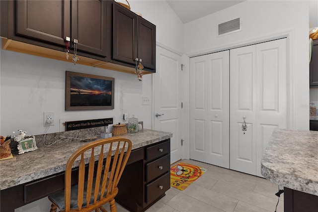 kitchen with dark brown cabinets, built in desk, light tile patterned floors, and vaulted ceiling