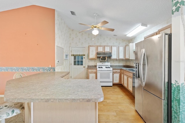 kitchen featuring a kitchen breakfast bar, vaulted ceiling, appliances with stainless steel finishes, light hardwood / wood-style floors, and kitchen peninsula