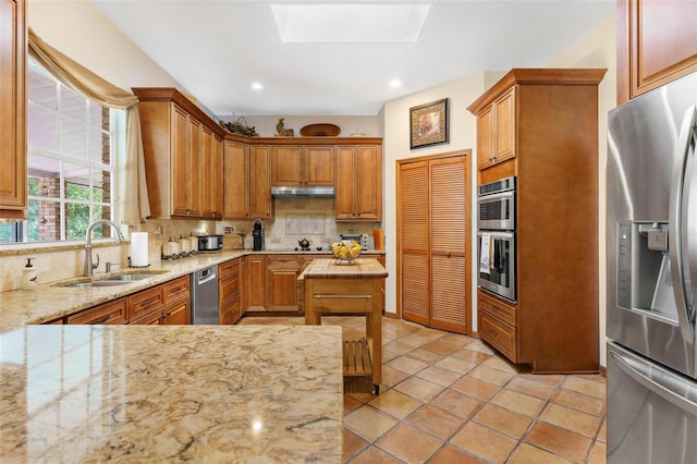 kitchen featuring backsplash, sink, a skylight, light stone countertops, and appliances with stainless steel finishes