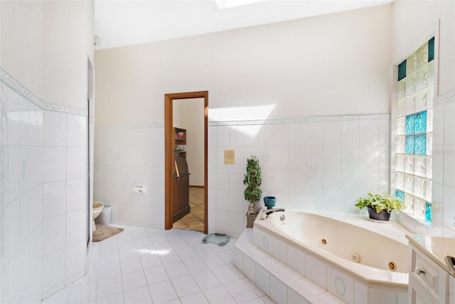 bathroom with vanity, tiled tub, tile walls, tile patterned flooring, and toilet