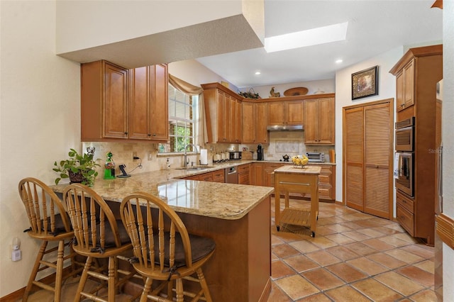 kitchen featuring a kitchen bar, kitchen peninsula, sink, and tasteful backsplash