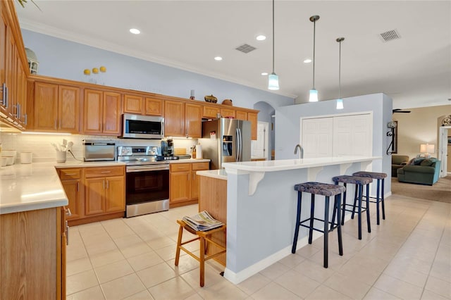 kitchen with appliances with stainless steel finishes, tasteful backsplash, light tile patterned floors, a center island with sink, and hanging light fixtures