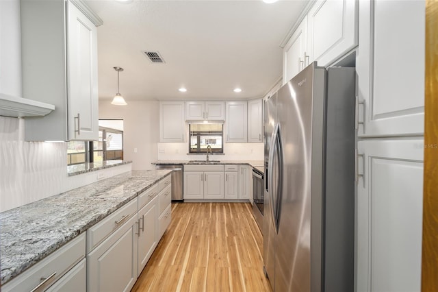 kitchen featuring white cabinetry, light stone counters, light hardwood / wood-style floors, pendant lighting, and appliances with stainless steel finishes