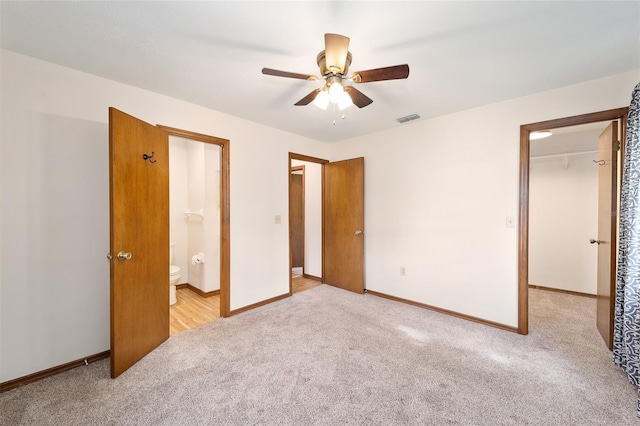 unfurnished bedroom with ensuite bath, a spacious closet, ceiling fan, light carpet, and a closet