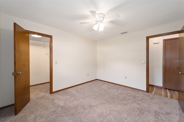 unfurnished bedroom featuring ceiling fan, a walk in closet, light carpet, and a closet